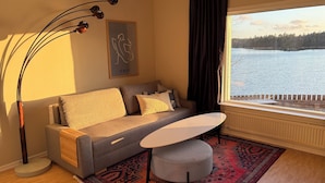 A cozy living room with a sofa, a small table, a patterned rug, and a view of a lake through a window. - Waterfront Guesthouse with Private Dock & Rowboat (Västra Götalands län)