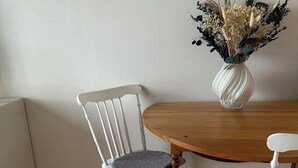 A dining area with a wooden table and two white chairs with grey cushions. A white vase with dried flowers is on the table. - Waterfront Guesthouse with Private Dock & Rowboat (Västra Götalands län)
