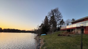 A lakeside property with a wooden deck, a glass-enclosed porch, and a view of the water. - Waterfront Guesthouse with Private Dock & Rowboat (Västra Götalands län)