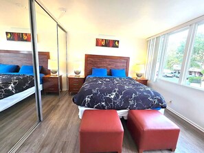 Ein modernes Hotelzimmer mit einem großen Bett, zwei Nachttischen, einem Spiegel und einem Fenster mit Blick ins Freie.