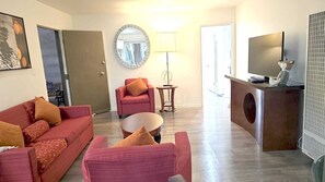 Ein Wohnzimmer mit einer Sofagarnitur, einem runden Spiegel, einem Fernseher und einem Schreibtisch.