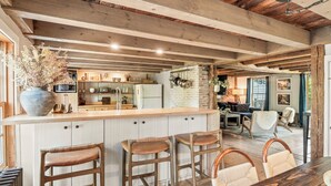 A rustic kitchen with a wooden island, bar stools, and a dining table with chairs. - Union Street Cottage - Built in 1900 (Hudson)