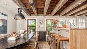 A modern kitchen with a wooden ceiling, a large island with stools, and a dining area with a dark wooden table and woven chairs. - Union Street Cottage - Built in 1900 (Hudson)