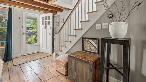 A wooden staircase with white railings leading to a door. A white vase with branches is on a black table beside the stairs. - Union Street Cottage - Built in 1900 (Hudson)