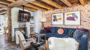 A cozy living room with a fireplace, a blue sofa, a wooden coffee table, and a white fur throw. - Union Street Cottage - Built in 1900 (Hudson)
