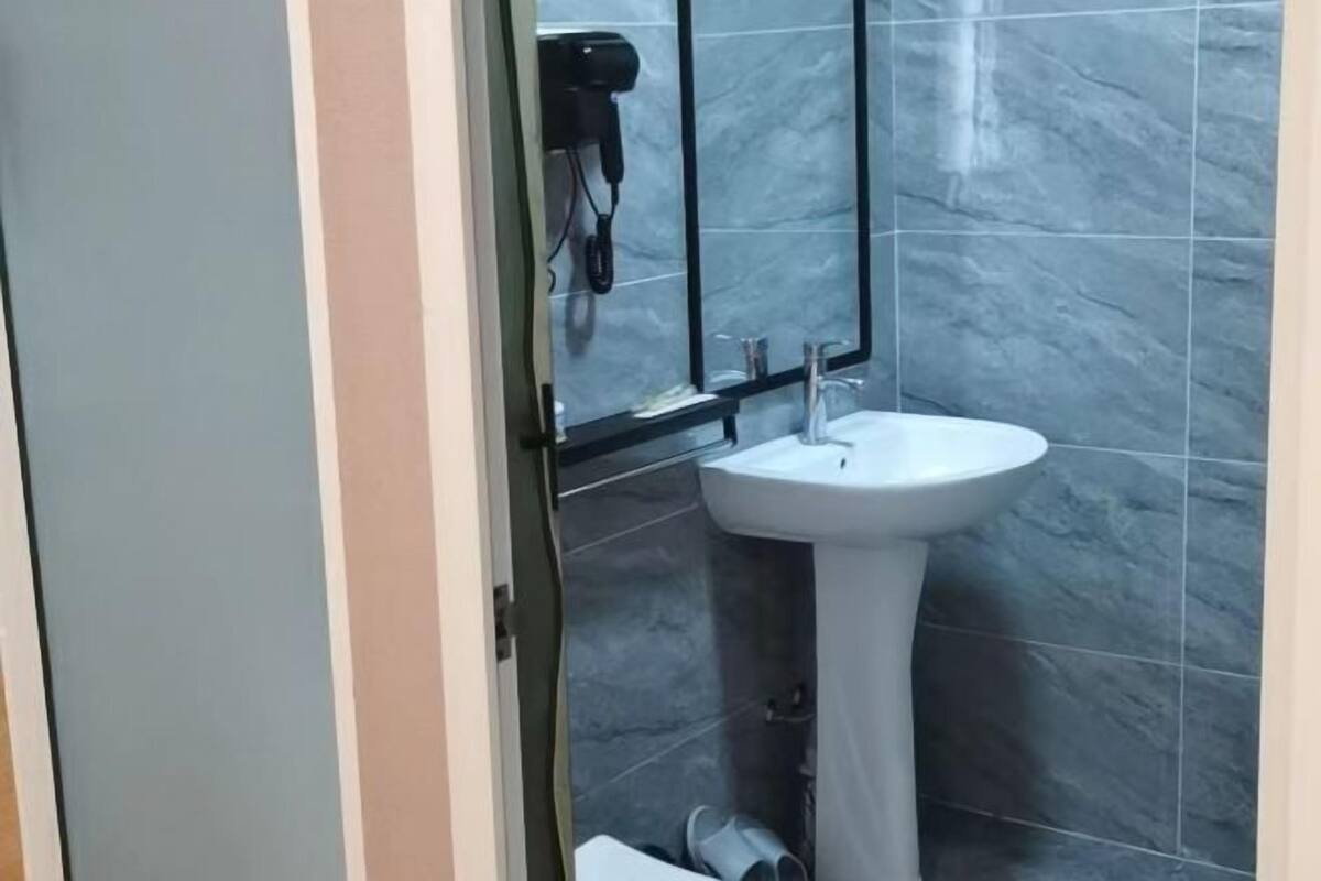 A bathroom with a pedestal sink, a mirror, and a hairdryer mounted on the wall.