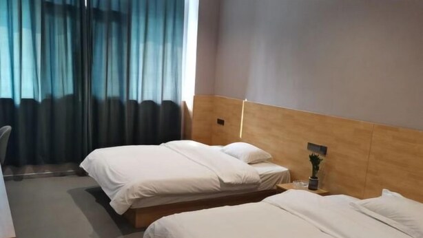A hotel room with two beds, a wooden headboard, a small table with a plant, and a window with curtains. - Apple Inn Express Hotel (Huantai)