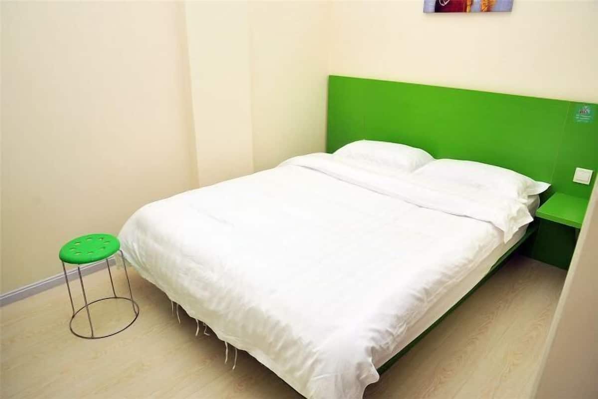 A single bed with a green headboard, a green stool, and a white pillow.