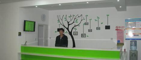 Una recepción con un mostrador verde, una pantalla digital en la pared y una decoración de árbol con elementos colgantes.