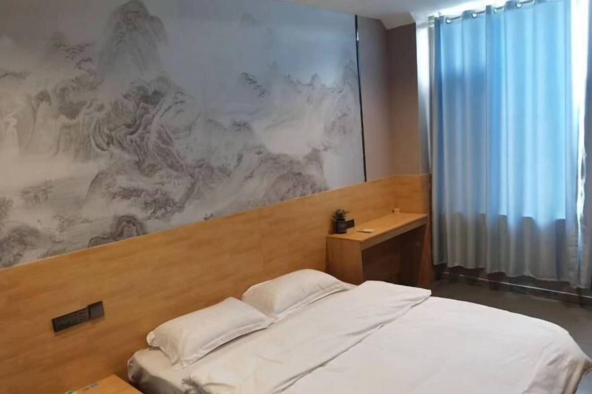A hotel room with a wooden headboard, a bed with white bedding, a small bedside table, and a wall with a traditional painting.