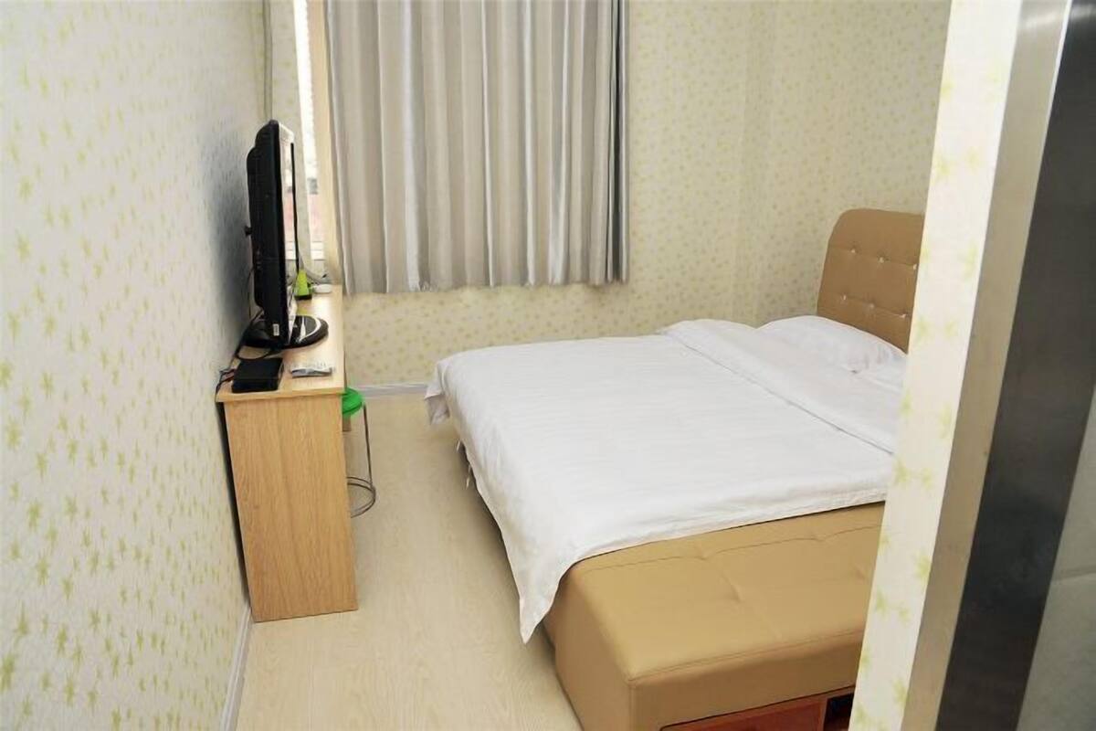 A hotel room with a bed, a desk with a television, and a window with curtains.