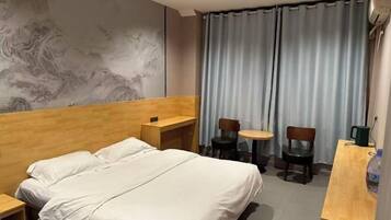 Een hotelkamer met een bed, een bureau, twee stoelen, een tafeltje en een gordijn.