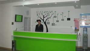 A reception desk with a green counter and a wall-mounted tree decoration. - Apple Inn Express Hotel (Huantai)