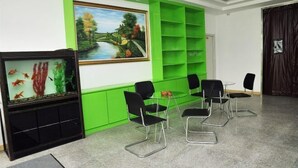 A room with a green accent wall, a painting of a landscape, a fish tank, and black chairs around a small table. - Apple Inn Express Hotel (Huantai)