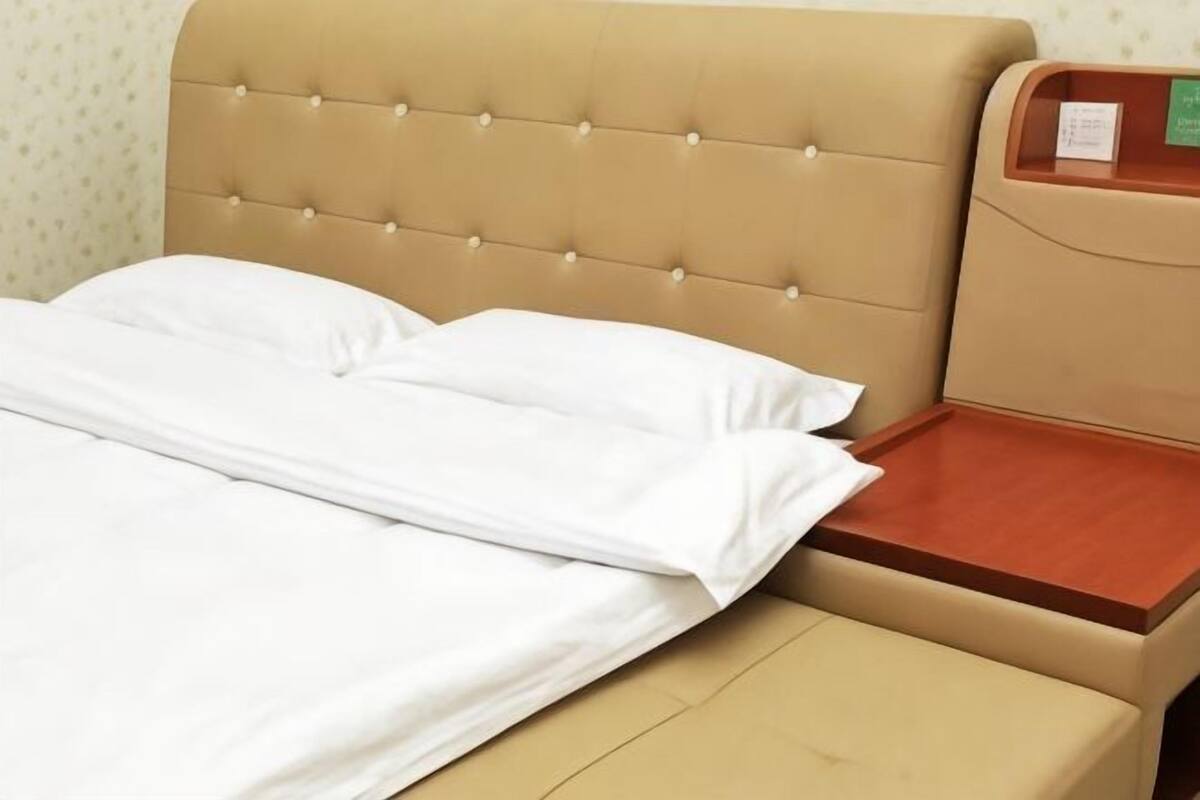 A bed with a headboard, a wooden bedside table, and a wall with a patterned wallpaper.
