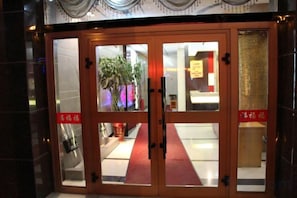 A hotel entrance with a red carpet, double doors, and a potted plant inside. - Luntai Tianbai Hotel (Luntai)