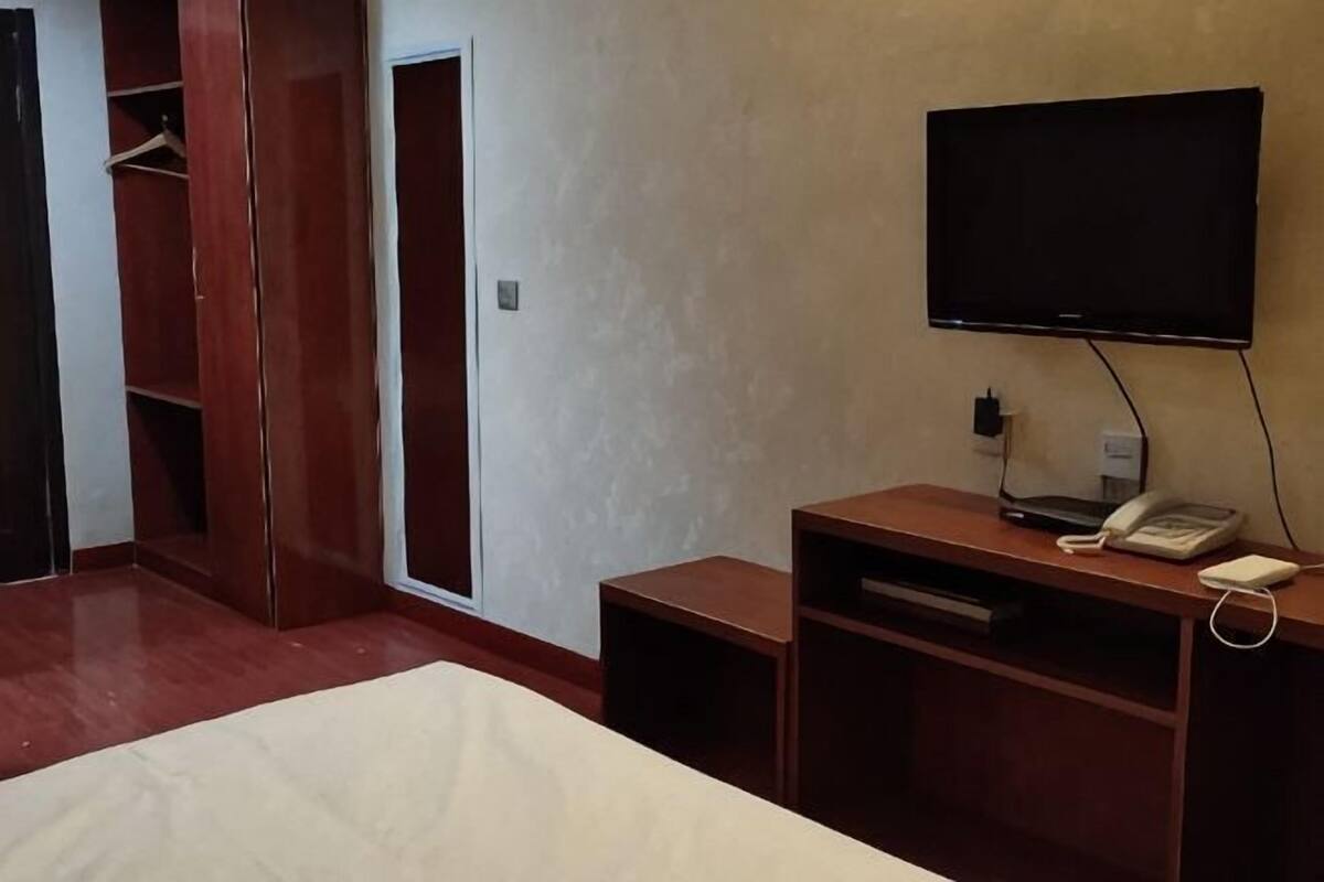 A hotel room with a bed, a TV mounted on the wall, a desk with a phone, and a wardrobe.