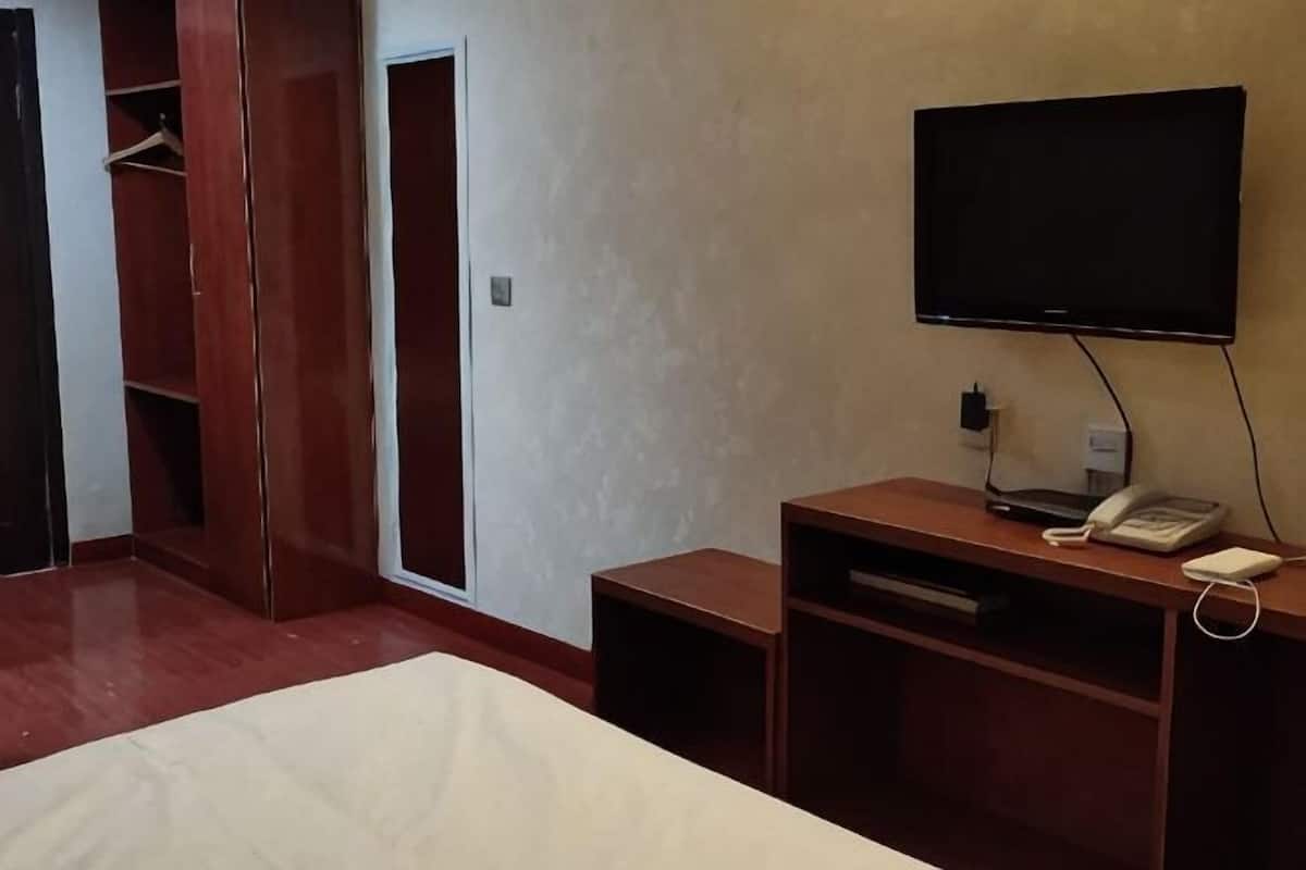 A hotel room with a bed, a TV mounted on the wall, a desk with a phone, and a wardrobe.