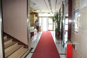 Vestíbulo de hotel con alfombra roja, una escalera y un mostrador de recepción.