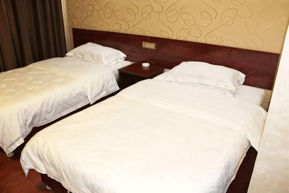 Two single beds with wooden headboards, a nightstand with a lamp, and a patterned wall.
