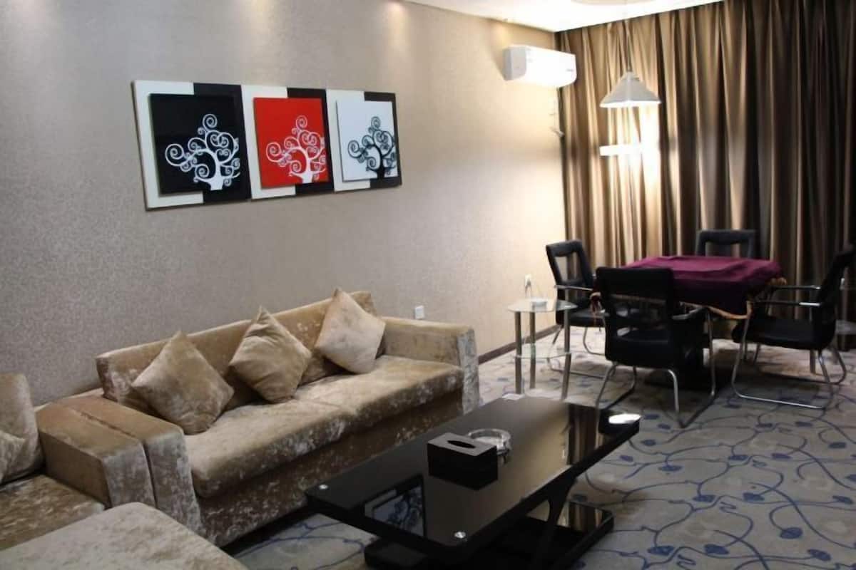 A hotel room with a sofa, a coffee table, a dining area with chairs, and three wall-mounted artworks.