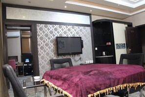 A hotel room with a bed, a TV mounted on the wall, a desk with a chair, and a wardrobe.