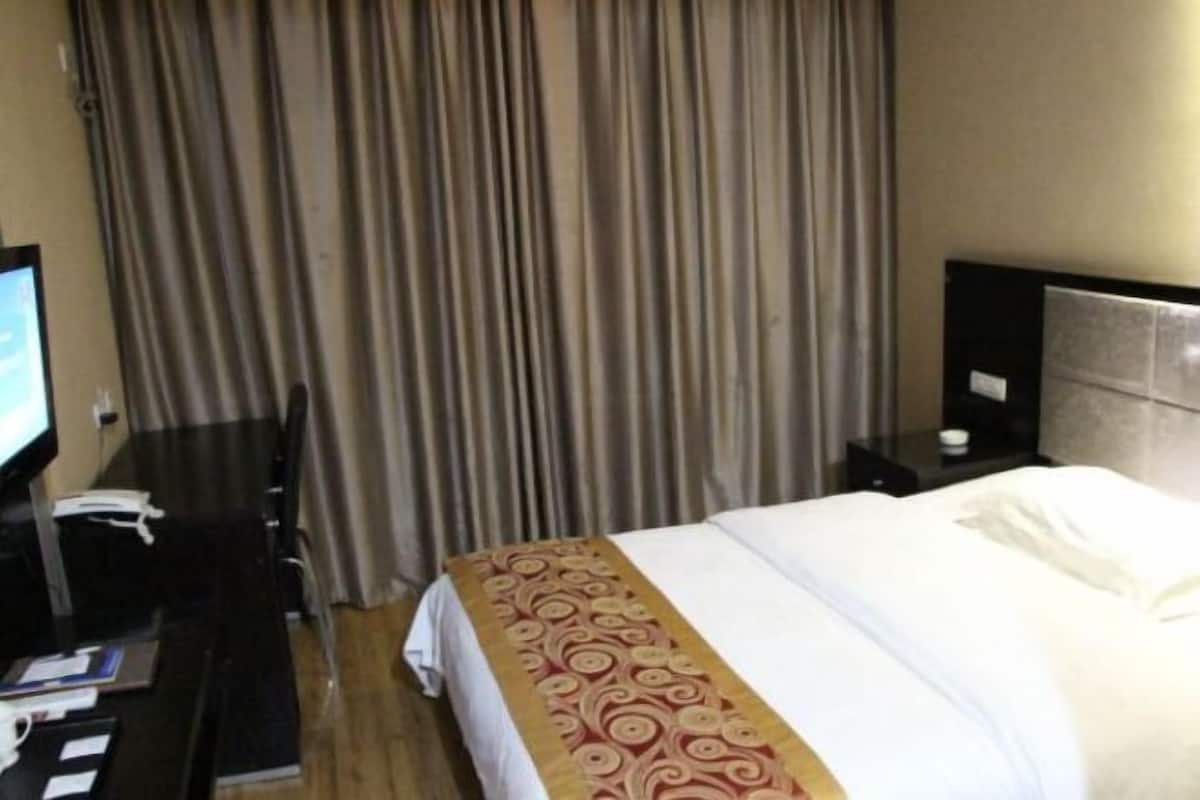 A hotel room with a bed, a desk with a telephone, a nightstand with a lamp, and a curtain.