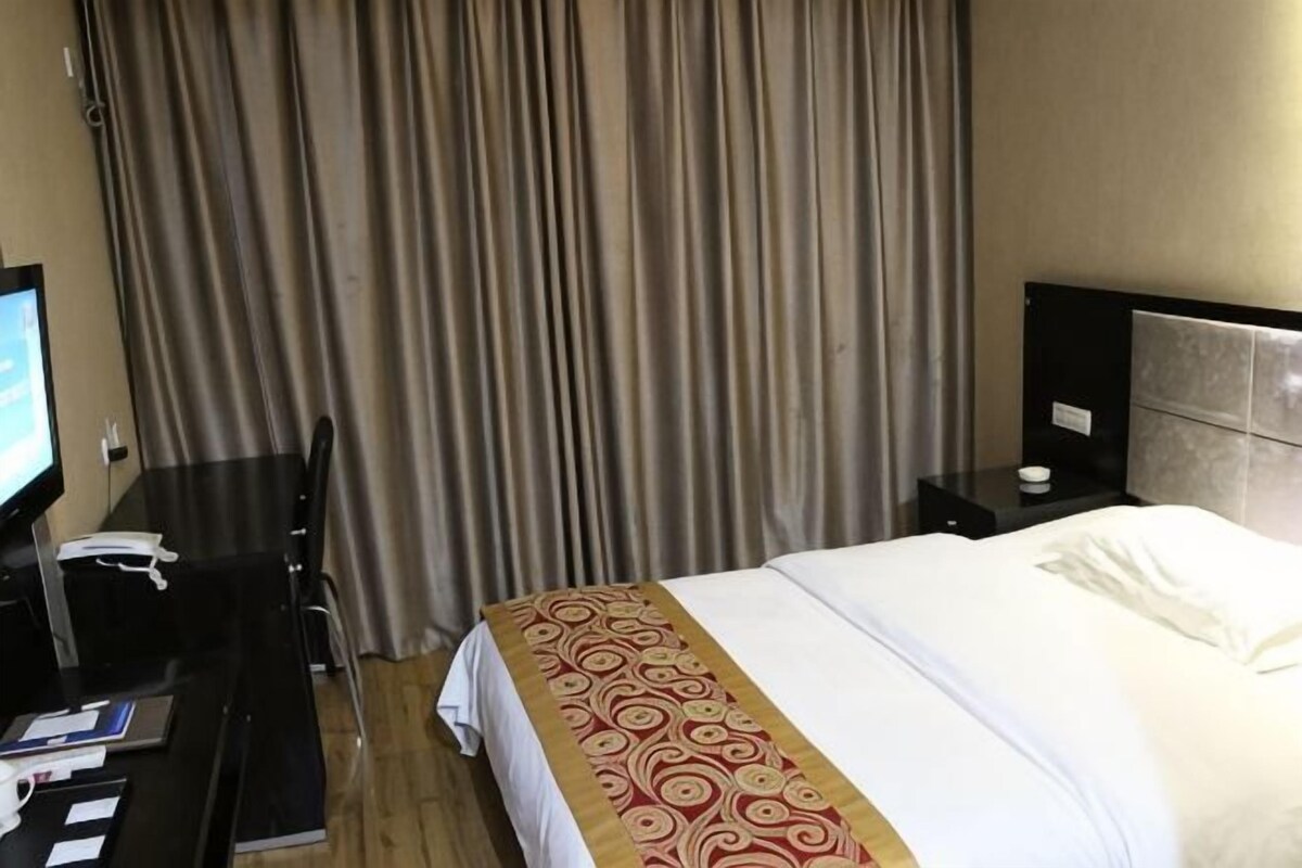 Une chambre d’hôtel avec un lit, un bureau, une télévision et des rideaux.