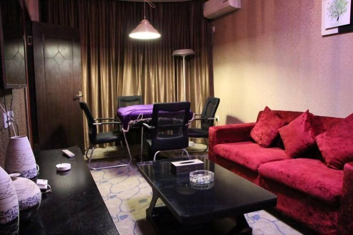 A room with a red sofa, a black coffee table, a purple chair, a desk with a lamp, and a curtain backdrop.