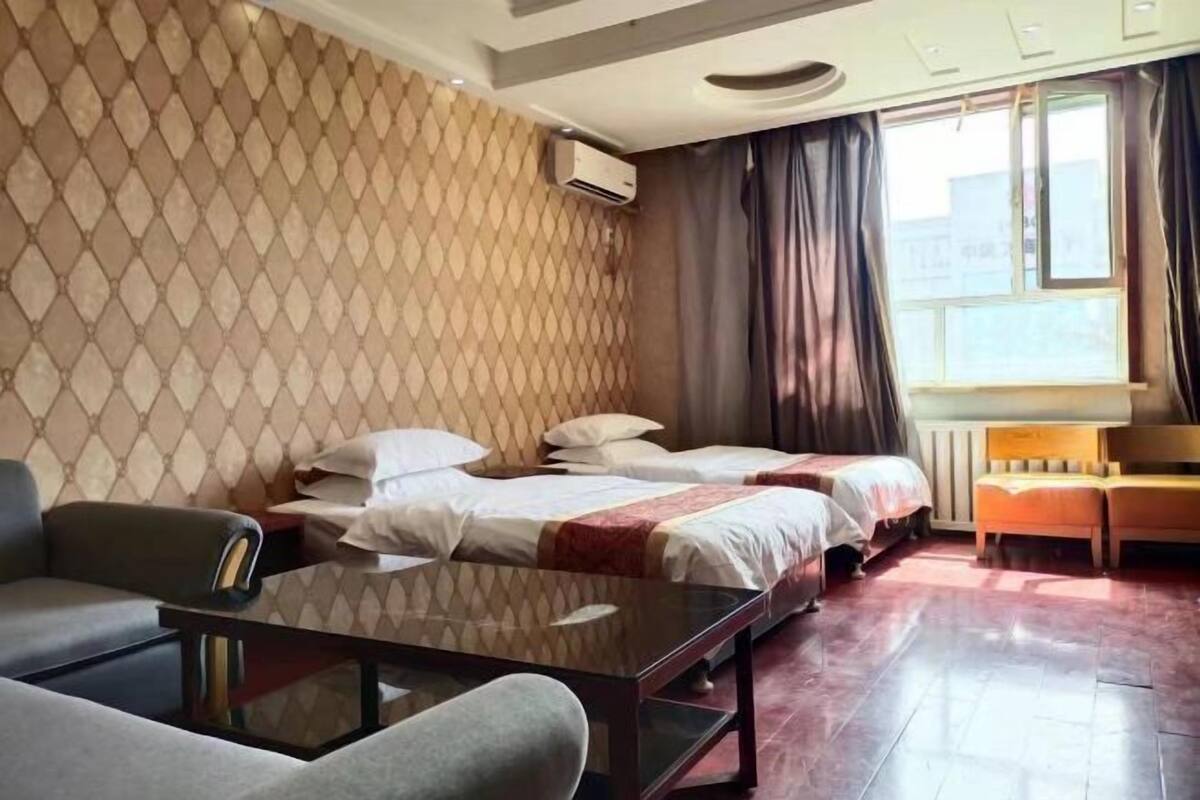 A hotel room with two beds, a sofa, a glass coffee table, and a window with curtains.