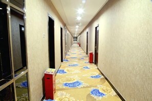 Un couloir d’hôtel avec un tapis à motifs floraux, des portes des deux côtés et une poubelle.