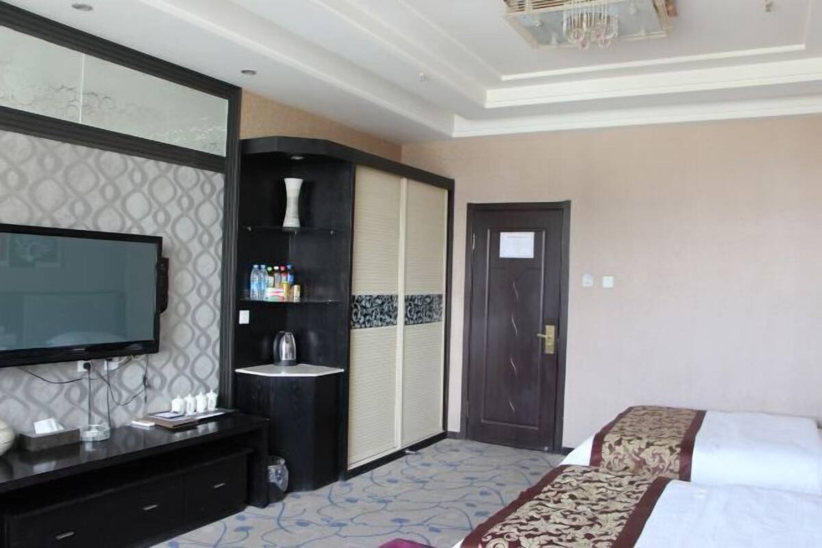 A hotel room with a large flat-screen TV, a black console with toiletries, a wardrobe, and a bed with a patterned bedspread.
