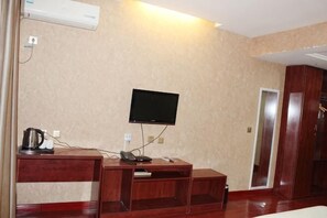Une chambre d’hôtel équipée d’un téléviseur à écran plat fixé au mur, d’un bureau en bois avec un téléphone et une machine à café, et d’une porte donnant sur une autre pièce.