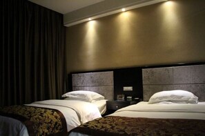 Une chambre d’hôtel avec deux lits, des rideaux foncés, une tête de lit dotée d’un luminaire et une table de chevet avec une lampe.