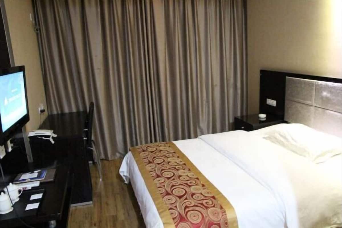 A hotel room with a bed, a desk with a computer, a telephone, and a television.