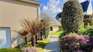 A residential pathway leading to a house with a garage, surrounded by well-maintained hedges and shrubs.