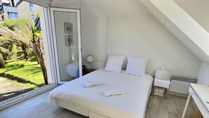 A bedroom with a large bed, a bedside table, a heater, and a view of a garden through a glass door.