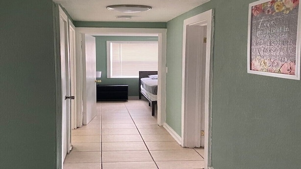 Un passadís amb un llit, una finestra amb persianes i una porta que dona a una altra habitació.