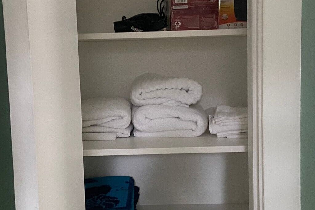 Een kast met planken, waarop witte handdoeken en een blauwe doos liggen.