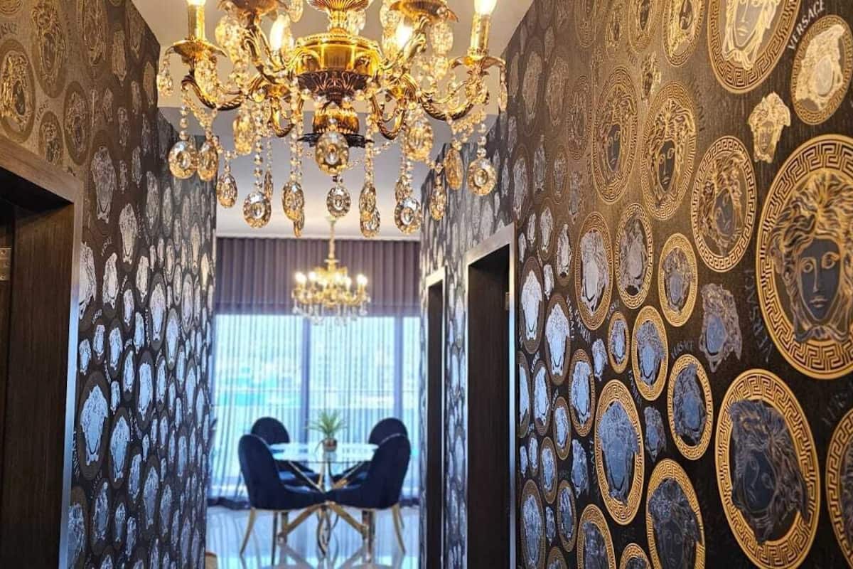 Ein Flur mit aufwendiger goldener und schwarzer Tapete, einer Chandelier und einem Essbereich mit zwei Stühlen und einem Tisch.