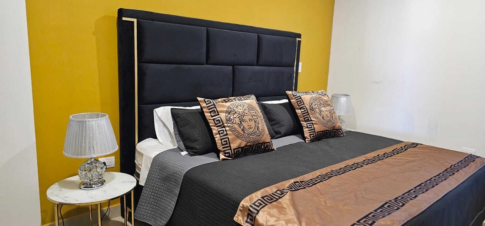 A bed with a black headboard, grey bedding, and decorative pillows with a geometric pattern.