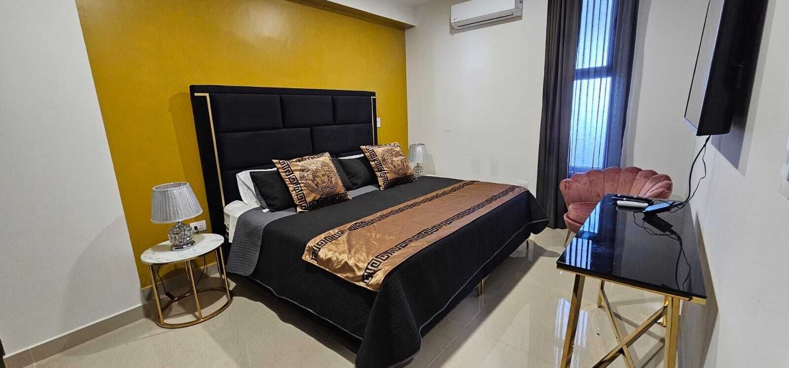 A hotel room with a bed, a desk, a chair, a lamp, and a TV.