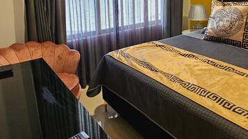 Una habitación de hotel con cama, escritorio con control remoto, silla y ventana con cortinas.