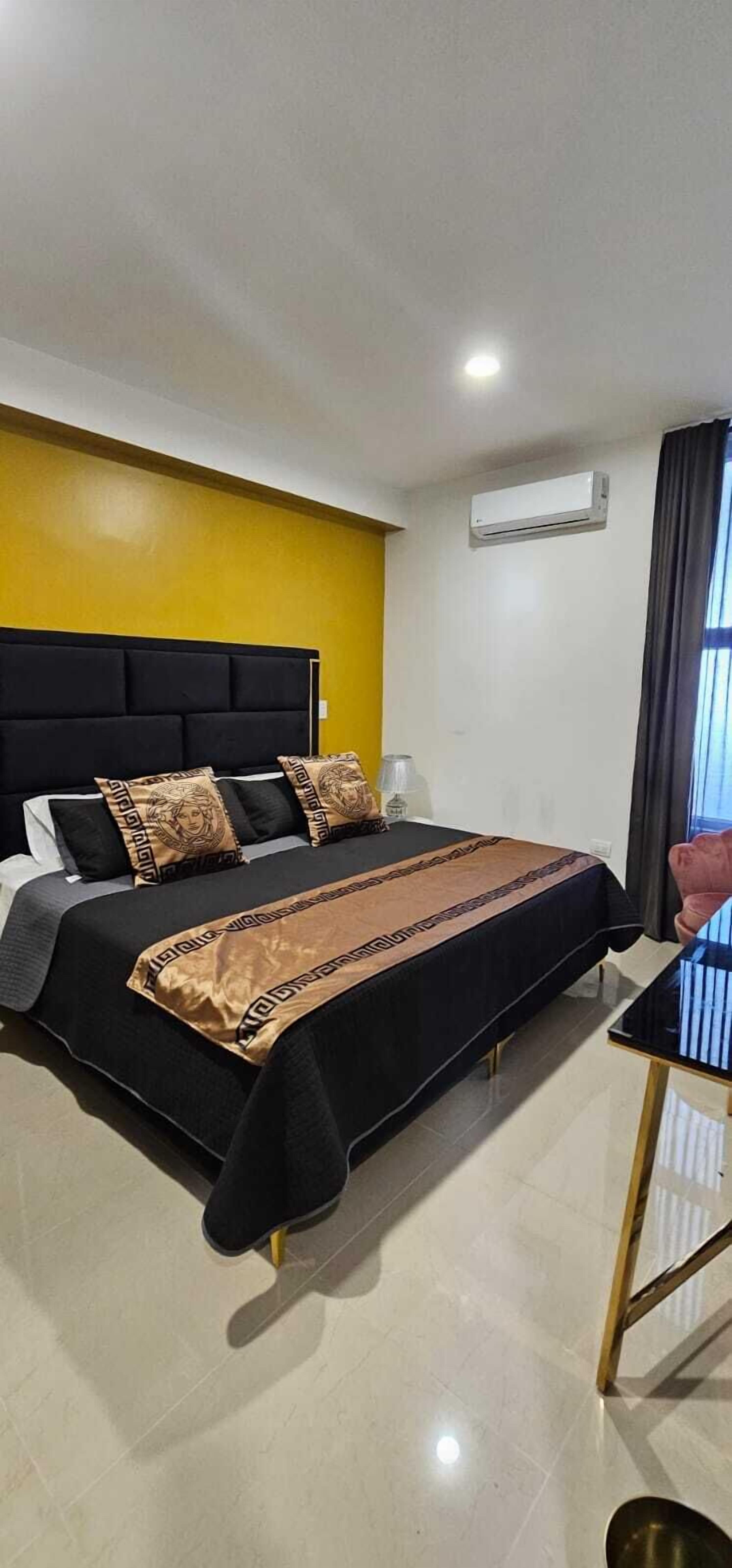 Une chambre d’hôtel comprenant un lit, une table de chevet, un appareil de climatisation et une fenêtre avec des rideaux.