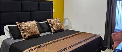 Une chambre d’hôtel comprenant un lit, une table de chevet, un appareil de climatisation et une fenêtre avec des rideaux.