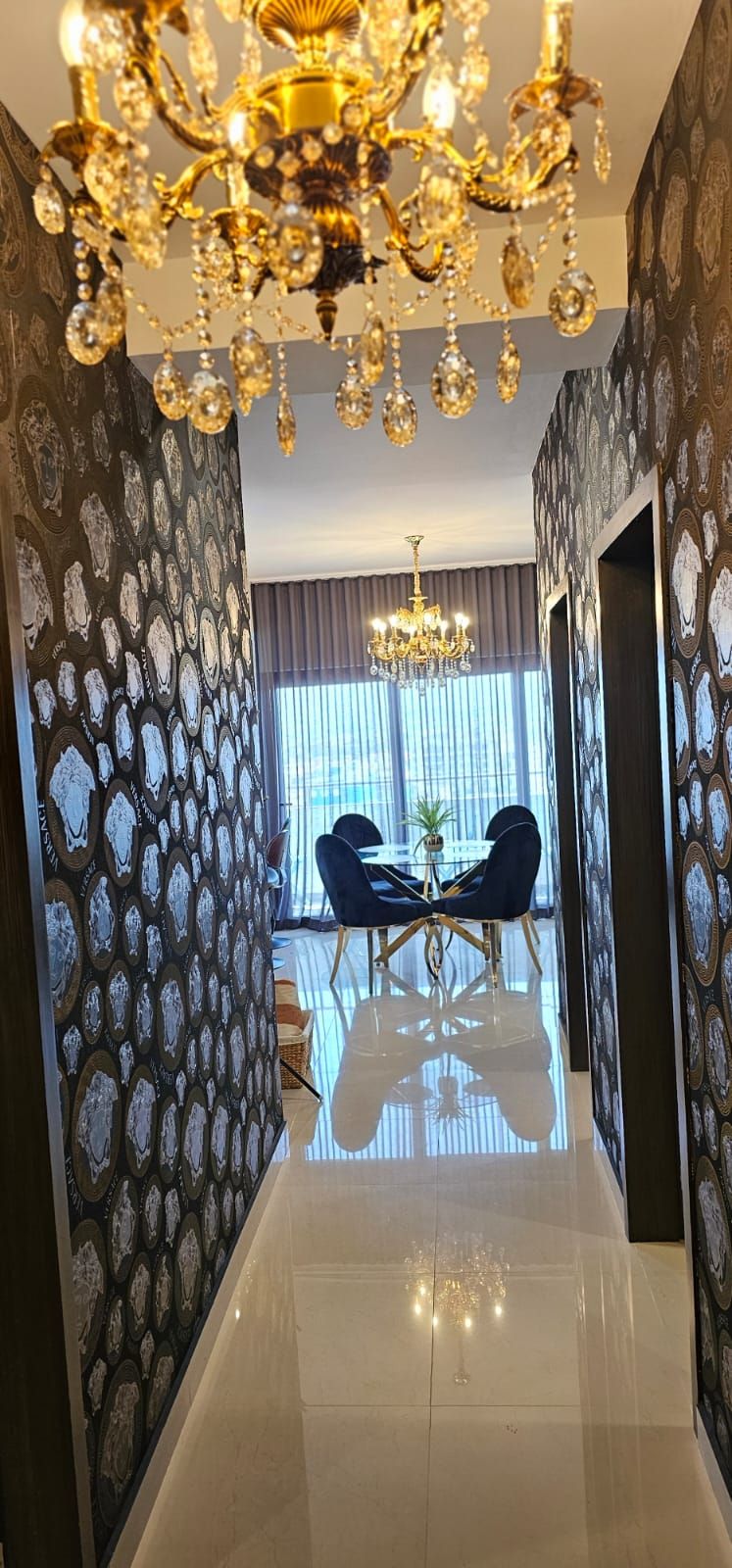 A hallway with a chandelier, patterned wallpaper, and a dining area with two chairs and a table.