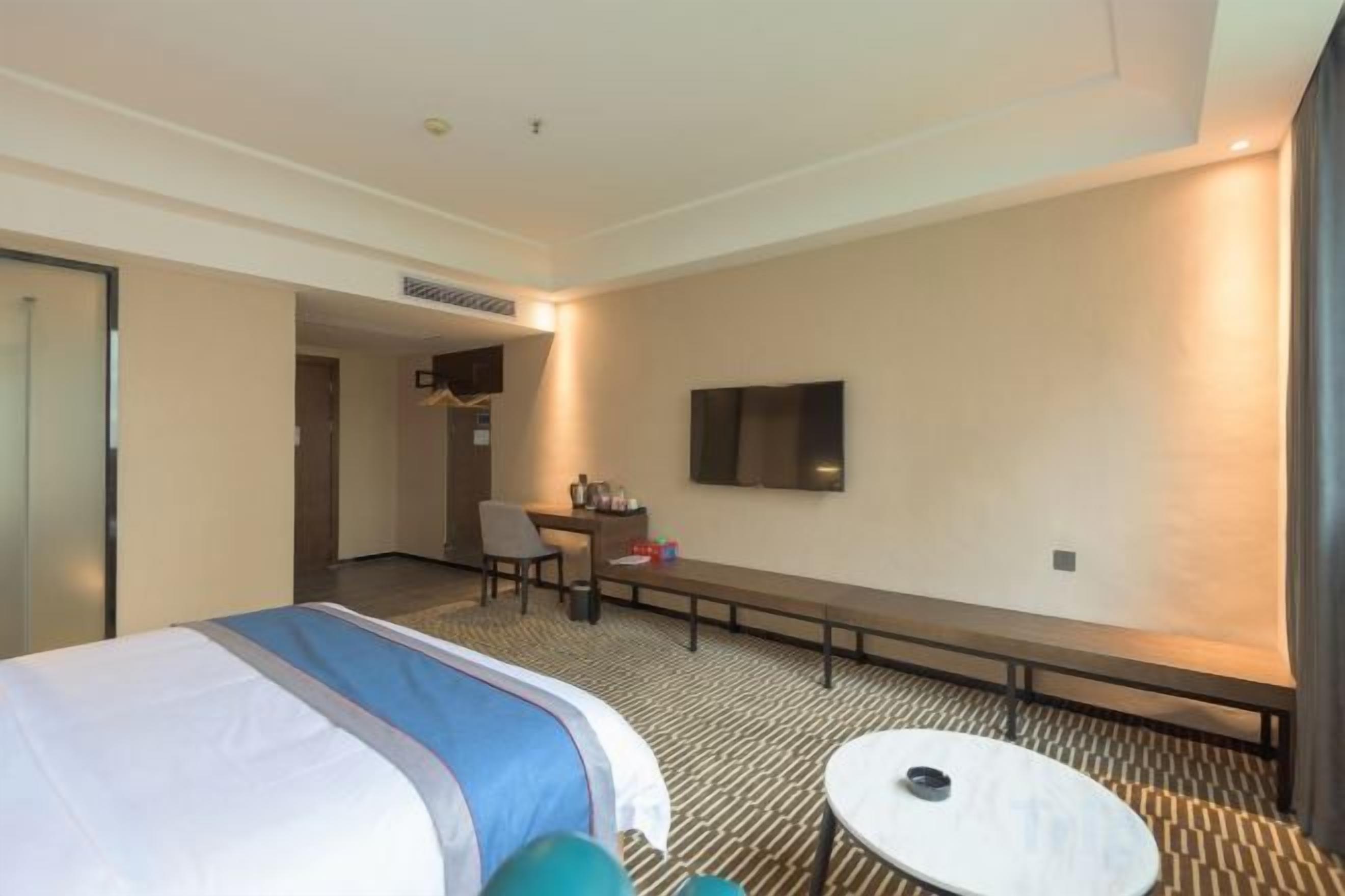 Ein Hotelzimmer mit Bett, Schreibtisch, Stuhl, Fernseher und einem kleinen runden Tisch.