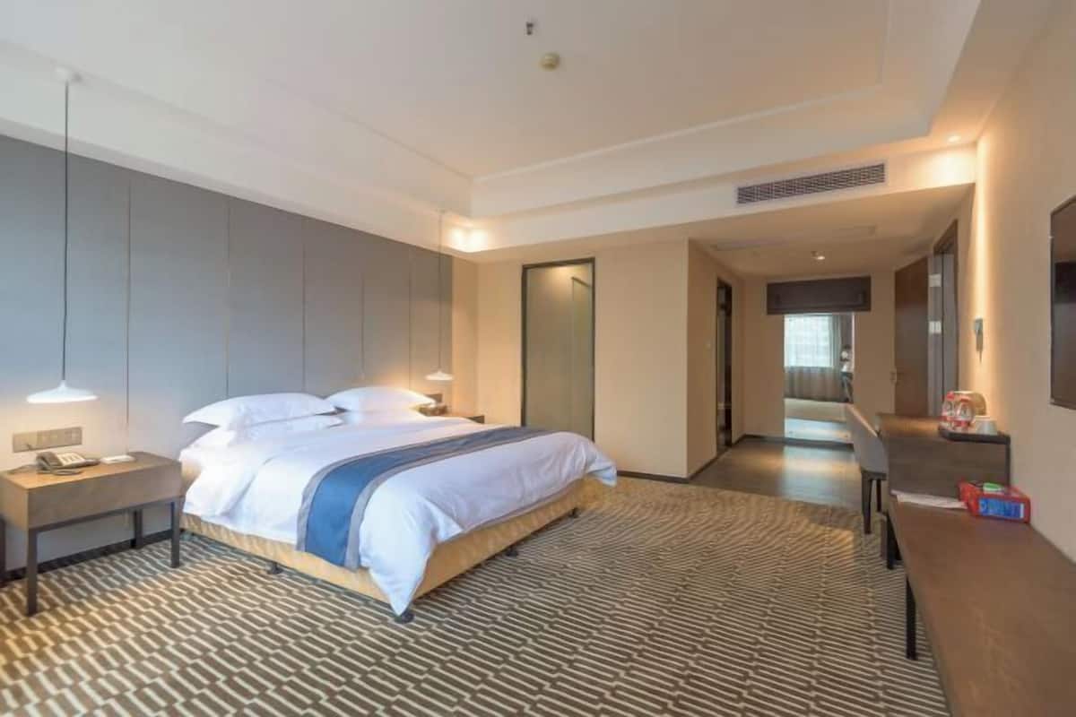 A modern hotel room with a large bed, bedside tables, a desk, and a flat-screen TV.