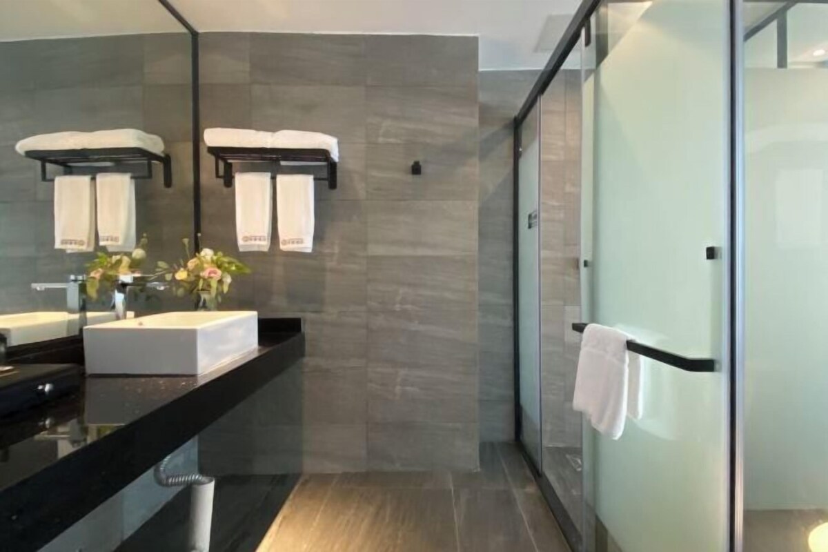 A modern bathroom with a large mirror, two towel racks, a black countertop, and a glass shower enclosure.