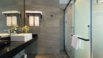 A modern bathroom with a large mirror, two towel racks, a black countertop, and a glass shower enclosure.